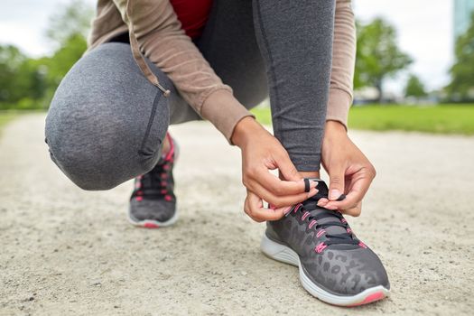 sport, fitness, people and lifestyle concept - close up of woman tying shoelaces outdoors