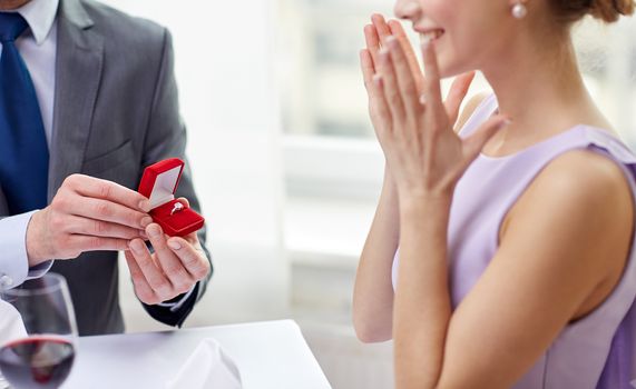 couple, love, engagement and holiday concept - close up of excited young woman and boyfriend giving her ring at restaurant