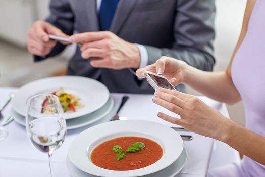 people, leisure, eating and technology concept - close up of couple with smartphones taking picture of food at restaurant