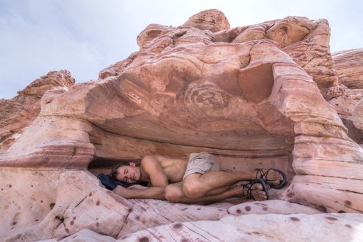 Handsome Caucasian hiker peacefully sleeps in shallow natural cave protected from hot desert sun in Red Rock Canyon, Las Vegas