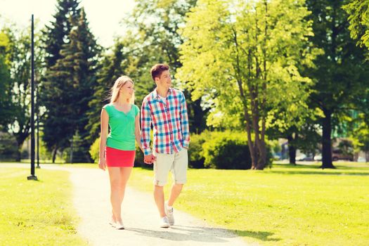 holidays, vacation, love and friendship concept - smiling couple walking and holding hands in park