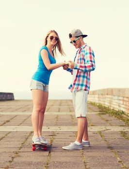holidays, vacation, love and friendship concept - smiling couple with skateboard riding outdoors