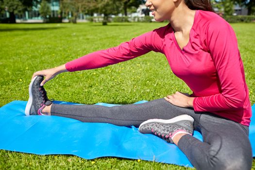 fitness, sport, training, people and lifestyle concept - close up of woman stretching leg on mat in park