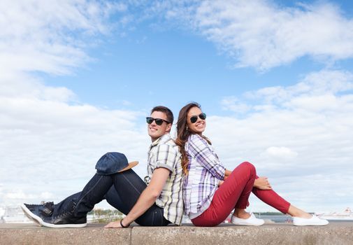 summer holidays and teenage concept - teenagers sitting back to back