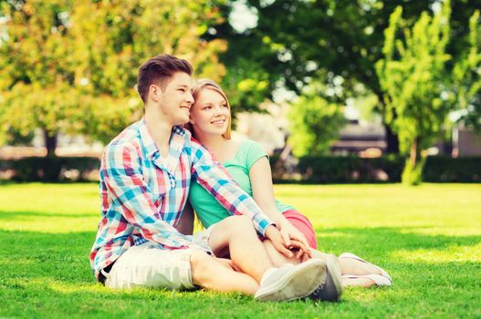 holidays, vacation, love and friendship concept - smiling couple sitting on grass in park