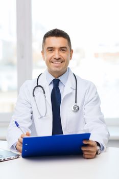 medicine, profession, technology and people concept - happy male doctor with clipboard in medical office