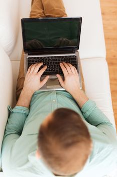 technology, leisure, advertisement and lifestyle concept - close up of man working with laptop computer and sitting on sofa at home