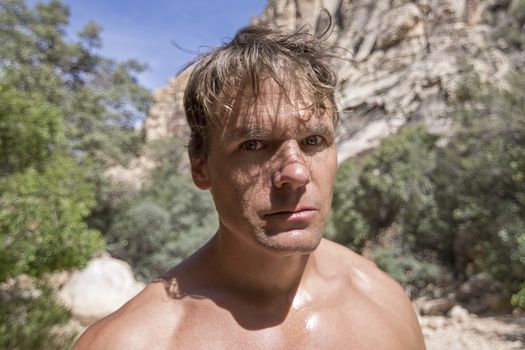 Closeup portrait of shirtless Caucasian man with crazy look in his eyes under sunny sky in natural wilderness environment