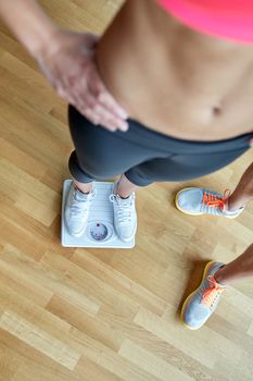 sport, fitness, slimming, weigh loss and people concept - close up of woman with personal trainer weighting on scales in gym