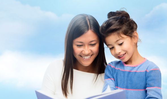 family, children, education, school and happy people concept - happy mother and daughter reading book over blue sky background