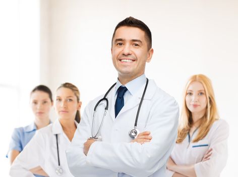 healthcare, profession, people and medicine concept - smiling male doctor in white coat over group of medics at hospital background