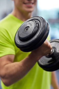 sport, fitness, lifestyle and people concept - close up of smiling man with dumbbell flexing biceps in gym