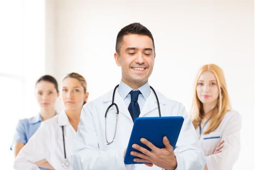 healthcare, profession, people and medicine concept - smiling male doctor in white coat with tablet pc over group of medics at hospital background