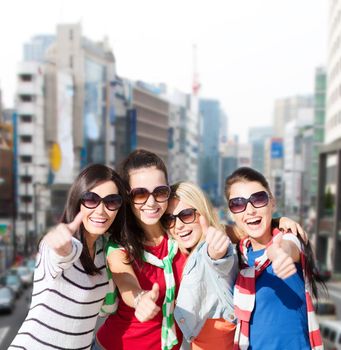 summer holidays, vacation and people concept - happy teenage girls in sunglasses or young students showing thumbs up over city background