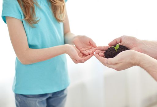 people, charity, family and care concept - close up of father and girl holding soil with green sprout in cupped hands at home