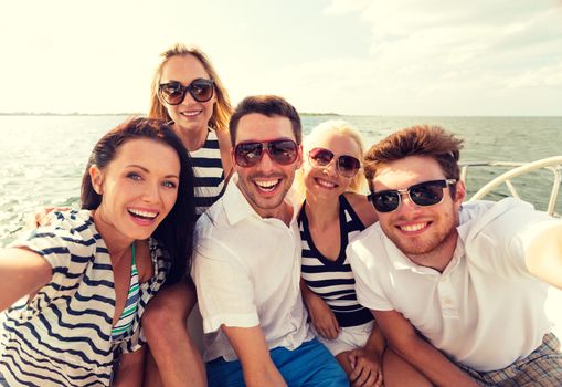 vacation, travel, sea, friendship and people concept - smiling friends sitting on yacht deck and making selfie