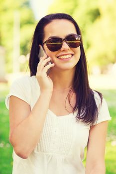 lifestyle, summer, vacation, technology and people concept - smiling young girl with smartphone calling in park