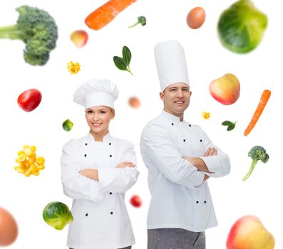 cooking, profession, vegetarian diet and people concept - happy chef couple or cooks with crossed hands over falling vegetables background