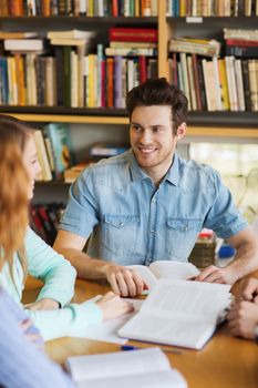 people, knowledge, education and school concept - group of happy students with books talking and preparing to exam in library