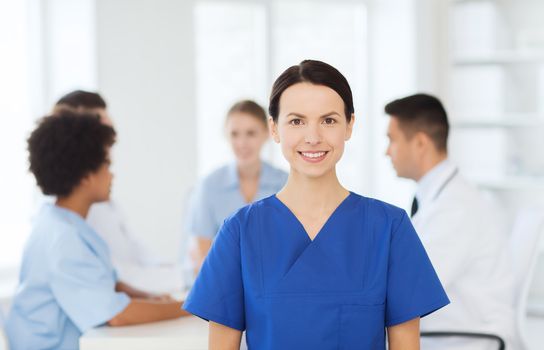 clinic, profession, people and medicine concept - happy female doctor or nurse over group of medics meeting at hospital