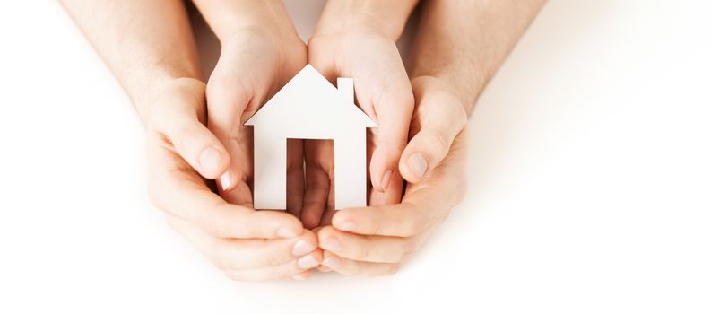 real estate and family home concept - closeup picture of male and female hands holding white blank paper house