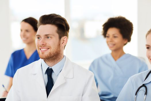 clinic, profession, people and medicine concept - happy male doctor over group of medics meeting at hospital