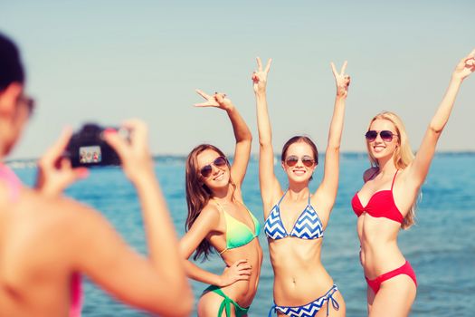 summer vacation, holidays, gesture and people concept - group of smiling women photographing by camera and showing peace sigh on beach