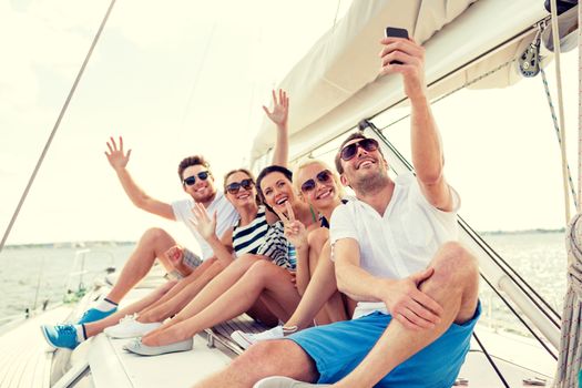 vacation, travel, sea, friendship and people concept - smiling friends sitting on yacht deck and making selfie