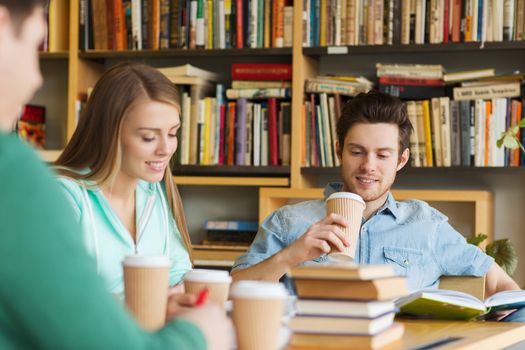 people, knowledge, education and school concept - group of happy students reading books, drinking coffee and preparing to exam in library