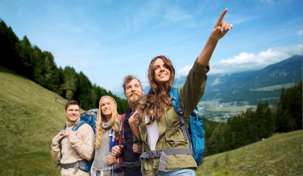 adventure, travel, tourism, hike and people concept - group of smiling friends with backpacks pointing finger over alpine hills background
