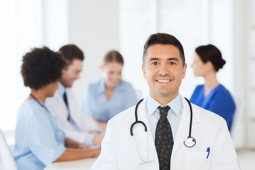 clinic, profession, people and medicine concept - happy male doctor over group of medics meeting at hospital