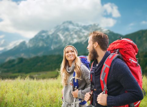 adventure, travel, tourism, hike and people concept - smiling couple walking with backpacks over alpine mountains background