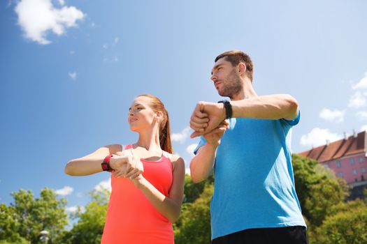 fitness, sport, training, technology and lifestyle concept - two smiling people with heart rate watches outdoors