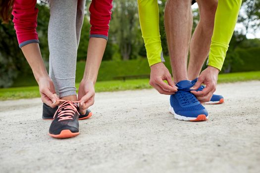 fitness, sport, friendship and lifestyle concept - close up of couple tying shoelaces outdoors