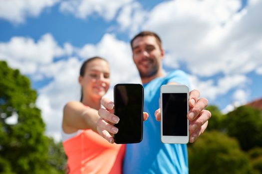 fitness, sport, training, technology and lifestyle concept - two smiling people with smartphones outdoors