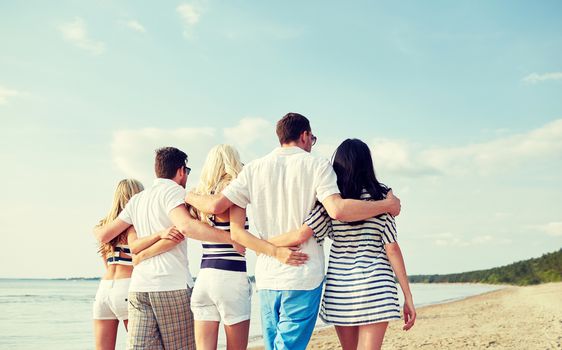 summer, holidays, sea, tourism and people concept - group of smiling friends hugging and walking on beach from back