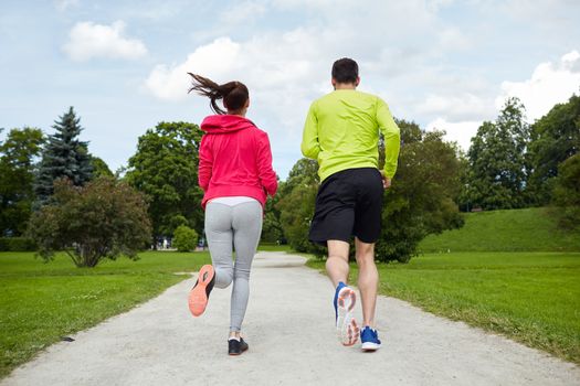 fitness, sport, friendship, people and lifestyle concept - smiling couple running outdoors from back