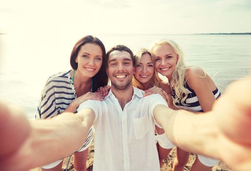 summer, sea, tourism, technology and people concept - group of smiling friends with camera on beach photographing and taking selfie