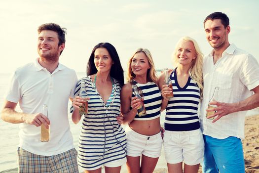 summer, holidays, tourism, drinks and people concept - group of smiling friends with bottles drinking beer or cider on beach