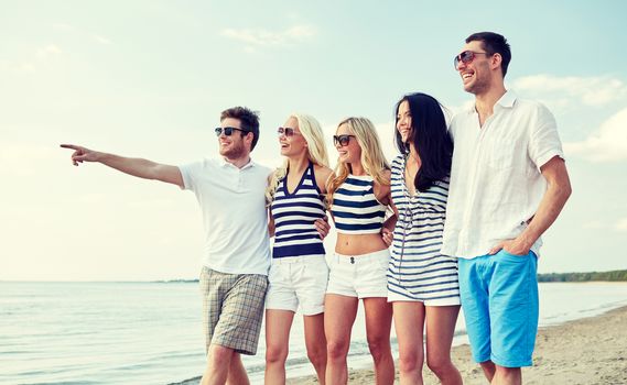 summer, holidays, sea, tourism and people concept - group of smiling friends in sunglasses walking on beach