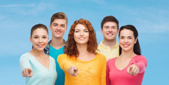 friendship, dream, future and people concept - group of smiling teenagers pointing fingers on you over blue sky with white cloud background