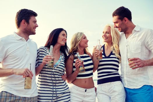 summer, holidays, tourism, drinks and people concept - group of smiling friends with bottles drinking beer or cider on beach