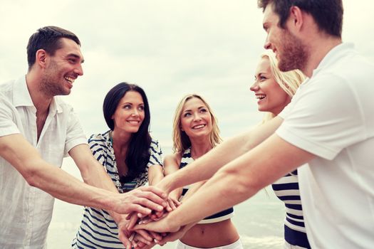 friendship, happiness, unity and people concept - smiling friends putting hands on top of each other