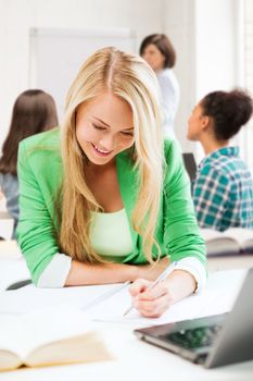 education and technology concept - smiling student girl writing in notebook at school