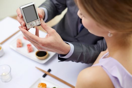 people, leisure, eating, food and technology concept - close up of couple with camera and sushi at restaurant
