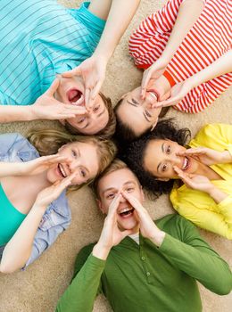 education and happiness concept - group of young smiling people lying down on floor in circle screaming and shouting