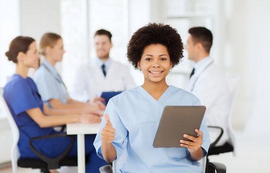 clinic, profession, people and medicine concept - happy female doctor with tablet pc computer over group of medics meeting at hospital showing thumbs up gesture