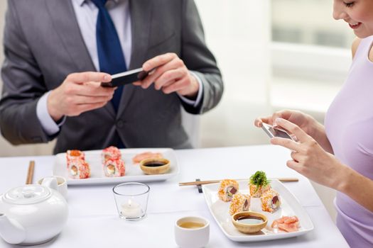 people, leisure, eating, food and technology concept - close up of couple with smartphones taking picture of sushi at restaurant