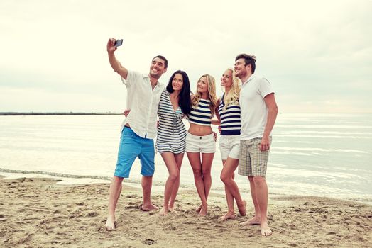 summer, sea, tourism, technology and people concept - group of smiling friends with smartphone on beach photographing and taking selfie