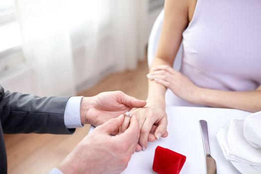 couple, love, engagement and holiday concept - close up of man putting ring to his fiance finger at restaurant